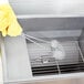 A person holding a Carlisle Sparta Spectrum fryer brush with looped Teflon bristles and cleaning a metal container.