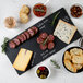 A rectangular black slate tray with various types of food, including meats, cheese, and soup.