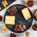 A variety of cheese and meat on an Acopa black slate tray on a table.