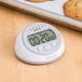 A Taylor digital kitchen timer with clock on a table with cookies.