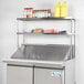 An Avantco stainless steel double deck overshelf on a counter over a stainless steel counter top.