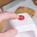 A person's finger pressing the red button on a white Cooper-Atkins kitchen timer.