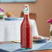 An Arcoroc tinted green glass bottle of red sauce sits on a table in a Mexican restaurant.