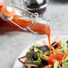 A hand pouring red sauce into an Arcoroc tinted green glass bottle.