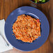 A plate of spaghetti with tomato sauce and a peacock blue melamine bowl of salad.