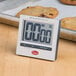 A Cooper-Atkins digital kitchen timer on a counter next to cookies.