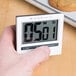 A person holding a Cooper-Atkins digital kitchen timer next to cookies on a counter.