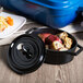 A black enamel oval pot with lid full of food on a table.