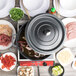 A GET gray enamel coated cast aluminum Dutch oven on a table with bowls of meat and green leaves.