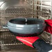 A person in red gloves holding a GET Heiss gray enamel coated cast aluminum brazier with a lid in an oven.