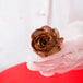 A gloved hand holding a chocolate frosting flower on a stainless steel Ateco flower nail.