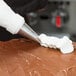 A person using an Ateco ruffle piping tip attached to a pastry bag to pipe white frosting on a brown cake.