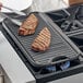 A pair of steaks cooking on a Valor cast iron grill pan.