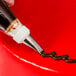 A pastry bag with brown frosting piped onto a red cake using an Ateco 3-hole piping tip.