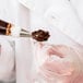 A person using an Ateco flat stainless steel flower nail to pipe chocolate frosting.