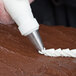 A hand using an Ateco drop flower piping tip with a pastry bag.