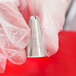 A hand in a glove holding a silver Ateco drop flower piping tip.