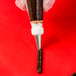 A white plastic Ateco leaf piping tip in a pastry bag with frosting on a red surface.