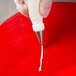 A hand using an Ateco open star piping tip to decorate a cake on a red plate.