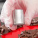 A hand in a glove holding a silver Ateco Russian piping tip.