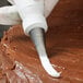 A person using an Ateco rose piping tip in a pastry bag to frost a cake.