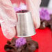 A person holding a silver metal Ateco Russian piping tip with a purple flower design.