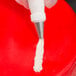 A hand holding a pastry bag with an Ateco closed star piping tip over a red surface.