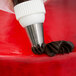 A person using an Ateco closed star pastry tip on a white and red pastry bag.