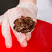 A person holding a spoon of chocolate frosting using an Ateco flat flower nail.