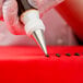 A person using an Ateco plain piping tip on a pastry bag to decorate a cake.