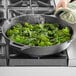 A hand cooking kale in a Valor cast iron skillet on a stovetop.