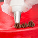 A hand using an Ateco Closed Star piping tip on a red cake.