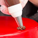 A person using an Ateco drop flower piping tip in a pastry bag to decorate a cake with chocolate.