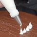 A person using an Ateco plain piping tip to pipe white frosting.