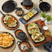 A table with a black Valor pre-seasoned cast iron skillet of fajitas, a black pot, and a bowl of food on it.