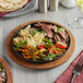 A Valor pre-seasoned cast iron fajita skillet with meat and vegetables on a table.