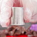 A person in a white glove using an Ateco Russian piping tip to pipe frosting onto a dessert.
