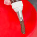 A hand holding a pastry bag with chocolate frosting using an Ateco curved petal piping tip.