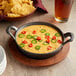 A Valor pre-seasoned cast iron round casserole dish filled with food on a table with a bowl of chips and a glass of beer.