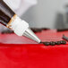 A person using an Ateco plain piping tip to pipe frosting onto a cake.