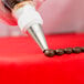 A person using an Ateco plain piping tip to pipe chocolate onto a table.