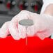 A person in white gloves using an Ateco stainless steel flower nail.