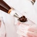 A person holding a pastry bag with chocolate frosting on a spoon.