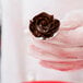 A person using an Ateco stainless steel flower nail to pipe chocolate frosting on a spoon.