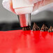 A person using an Ateco Christmas tree piping tip on a red surface.