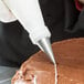 A person using an Ateco pastry bag with a plain tip to decorate a cake.