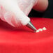 A hand using an Ateco curved petal piping tip in a pastry bag over a red surface.