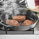 A person using Valor pre-seasoned cast iron skillet to cook meat on a stove.