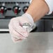 A person's gloved hand holding an Ateco stainless steel flower nail.