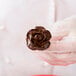 A hand holding a chocolate flower using an Ateco flat stainless steel flower nail.